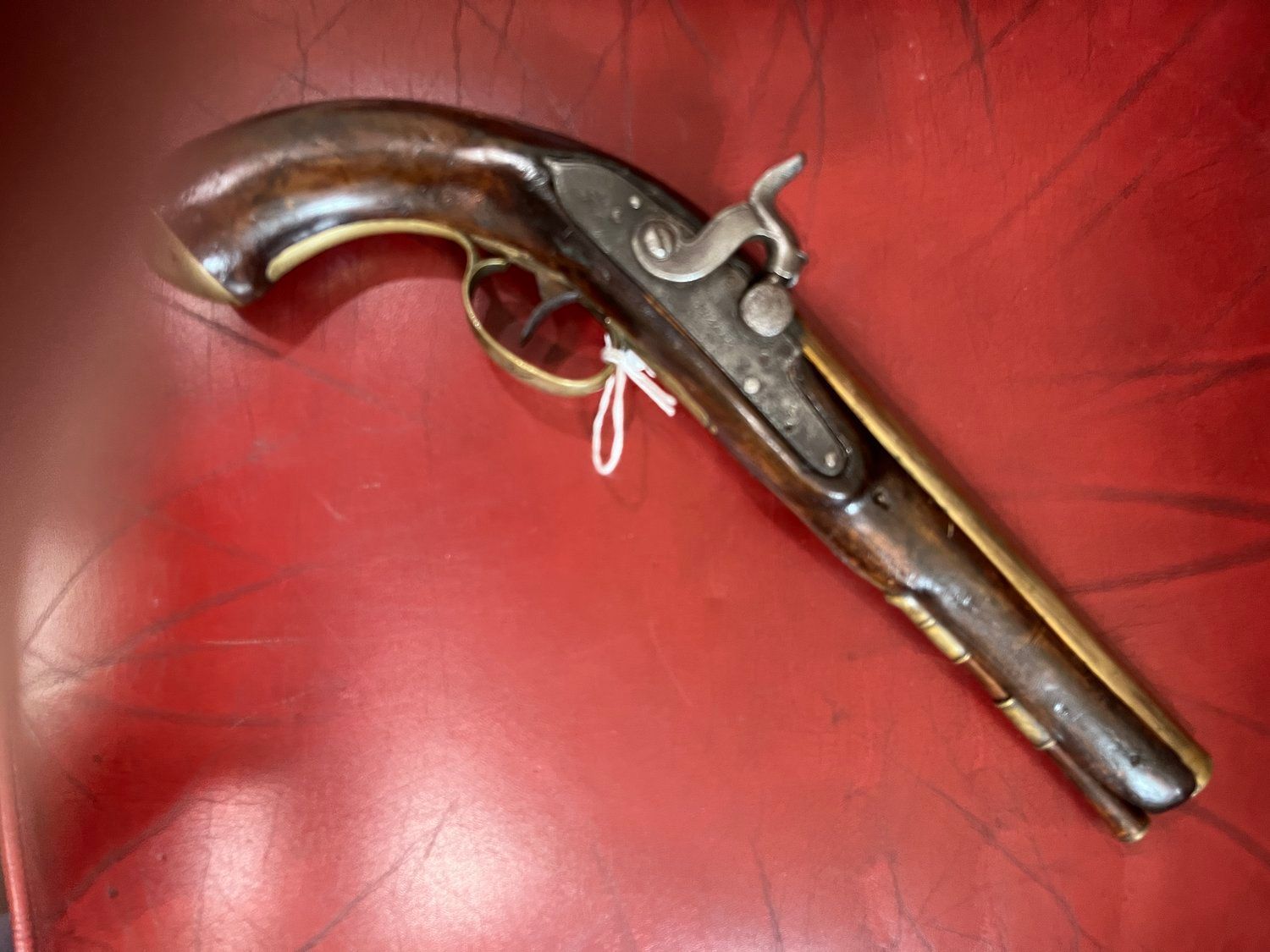 Antique flintlock pistol with a dark wooden handle and brass accents, resting on a red surface.