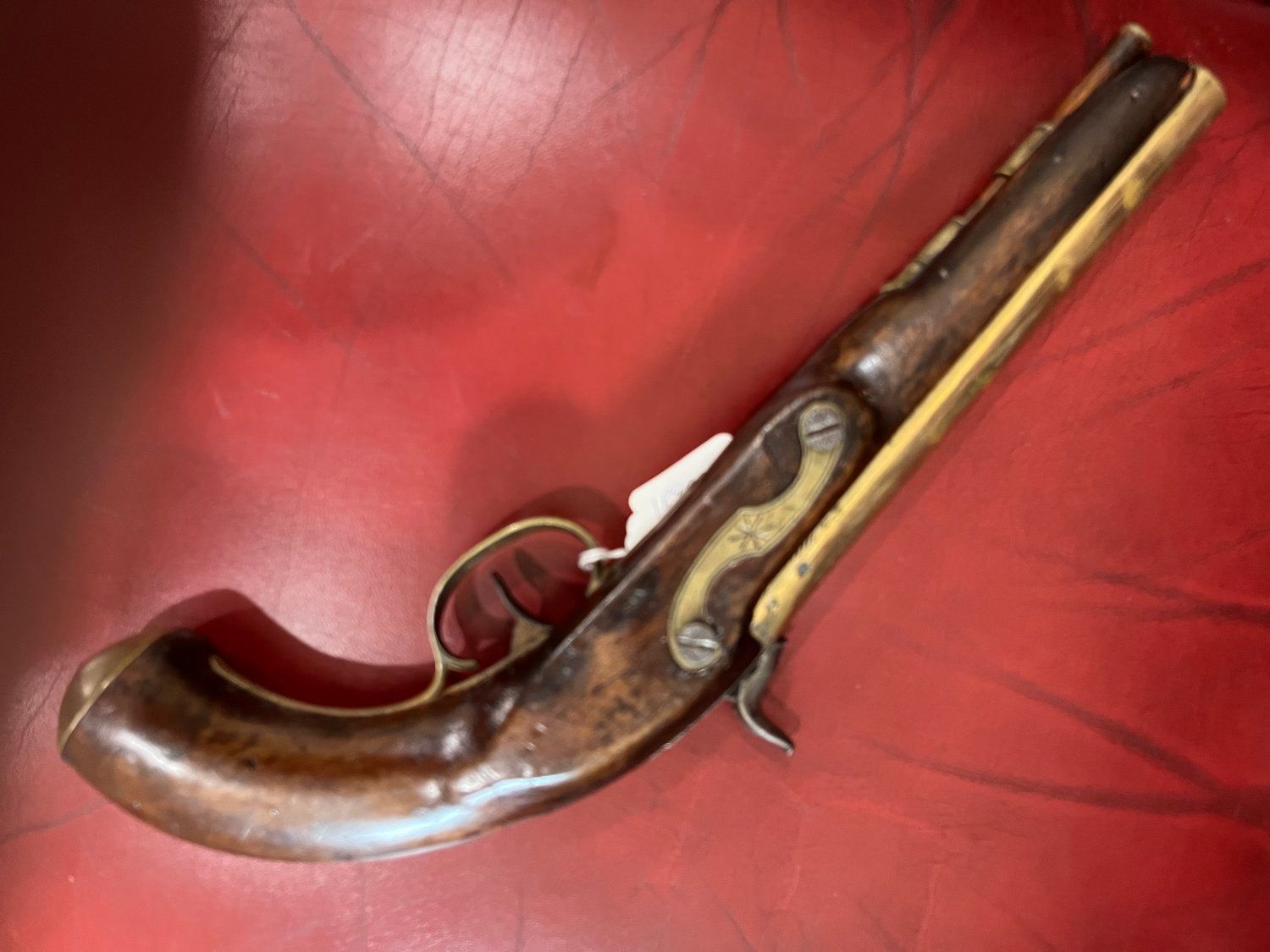Antique flintlock pistol with a dark wooden handle and brass accents, resting on a red surface.