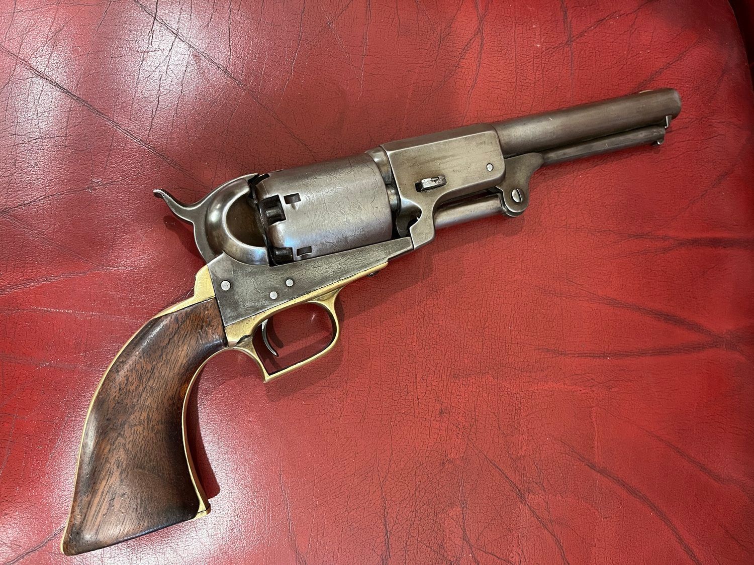 A revolver is sitting on a red leather couch.