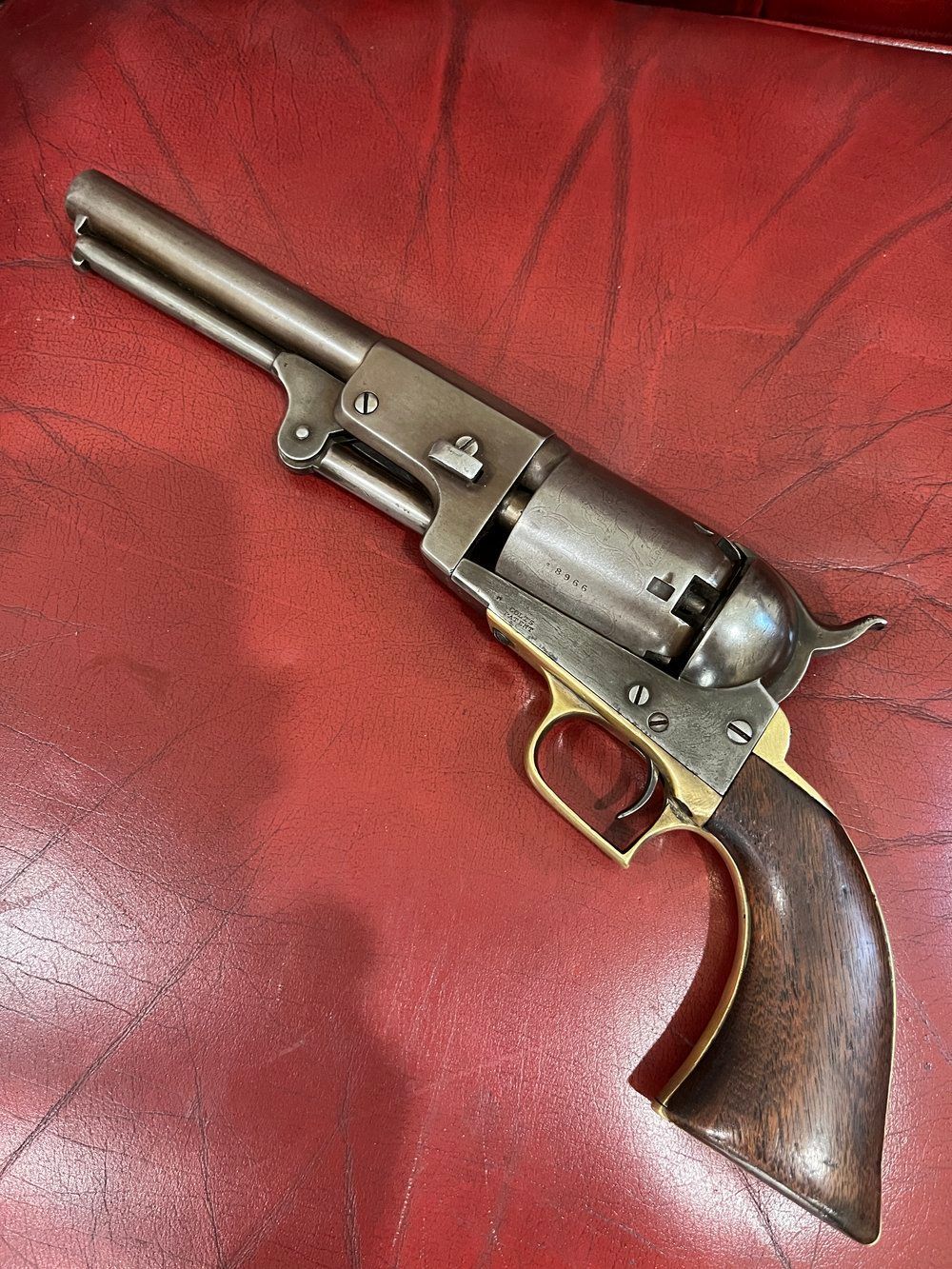 A revolver is sitting on a red leather couch.