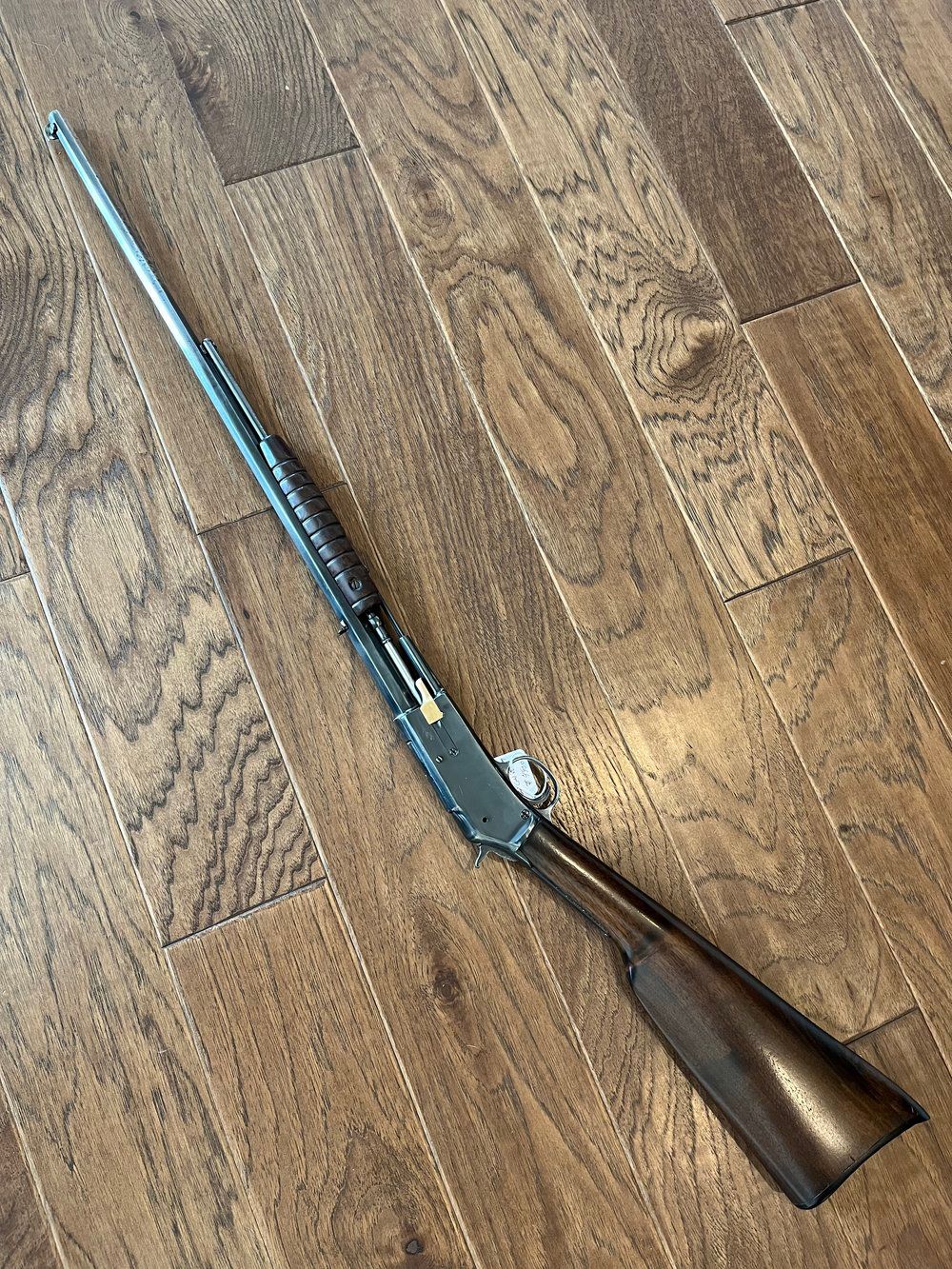 A rifle with a wooden stock and a long barrel rests on a wood floor.