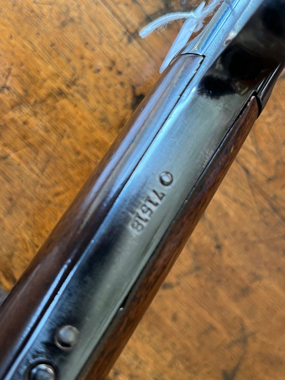 A rifle with a wooden stock and a long barrel rests on a wood floor.