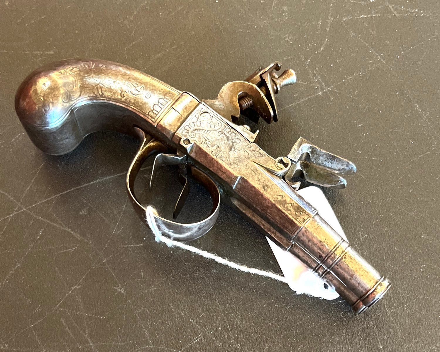 A vintage, ornate pistol with a curved handle rests on a dark surface. The gun is metallic with intricate engravings.
