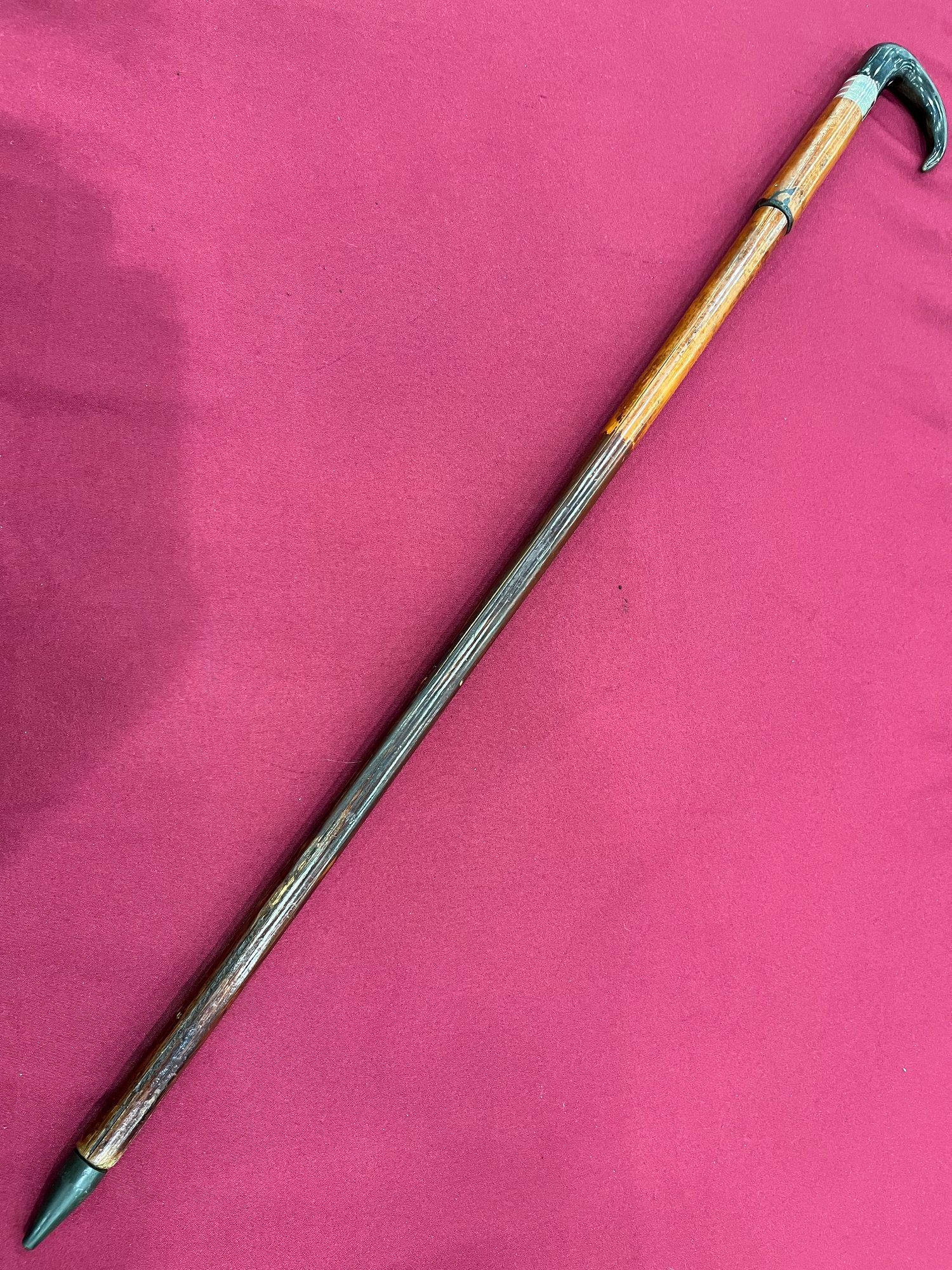 A cane with a snake handle is sitting on a pink cloth.