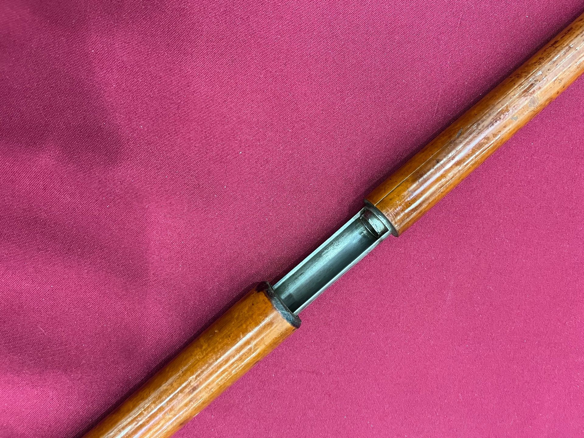 A cane with a snake handle is sitting on a pink cloth.