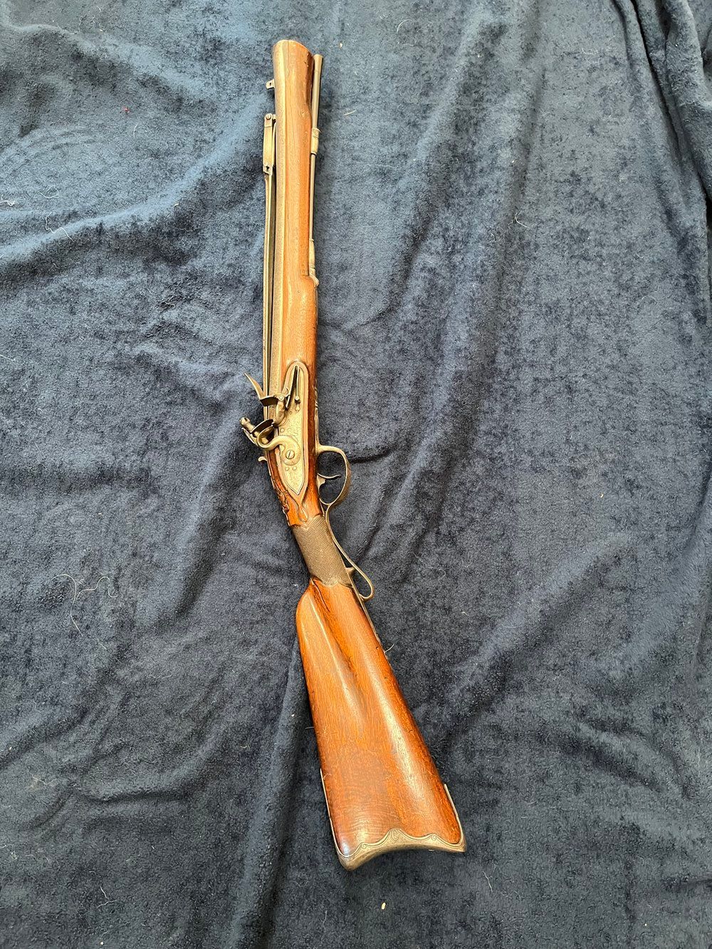 A brown and gold antique firearm with a leather wrapped stock on a dark blue textured surface.