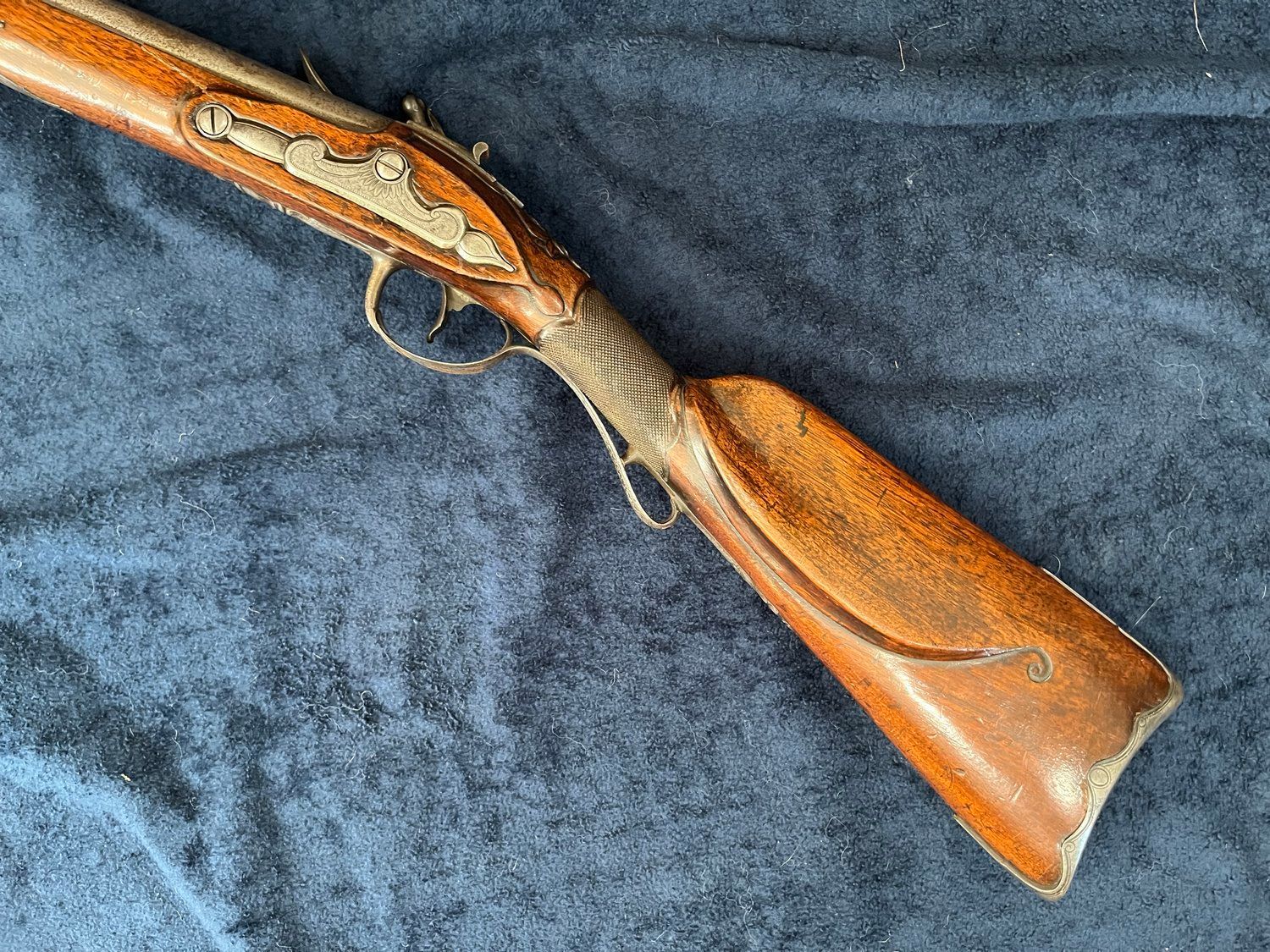A brown and gold antique firearm with a leather wrapped stock on a dark blue textured surface.