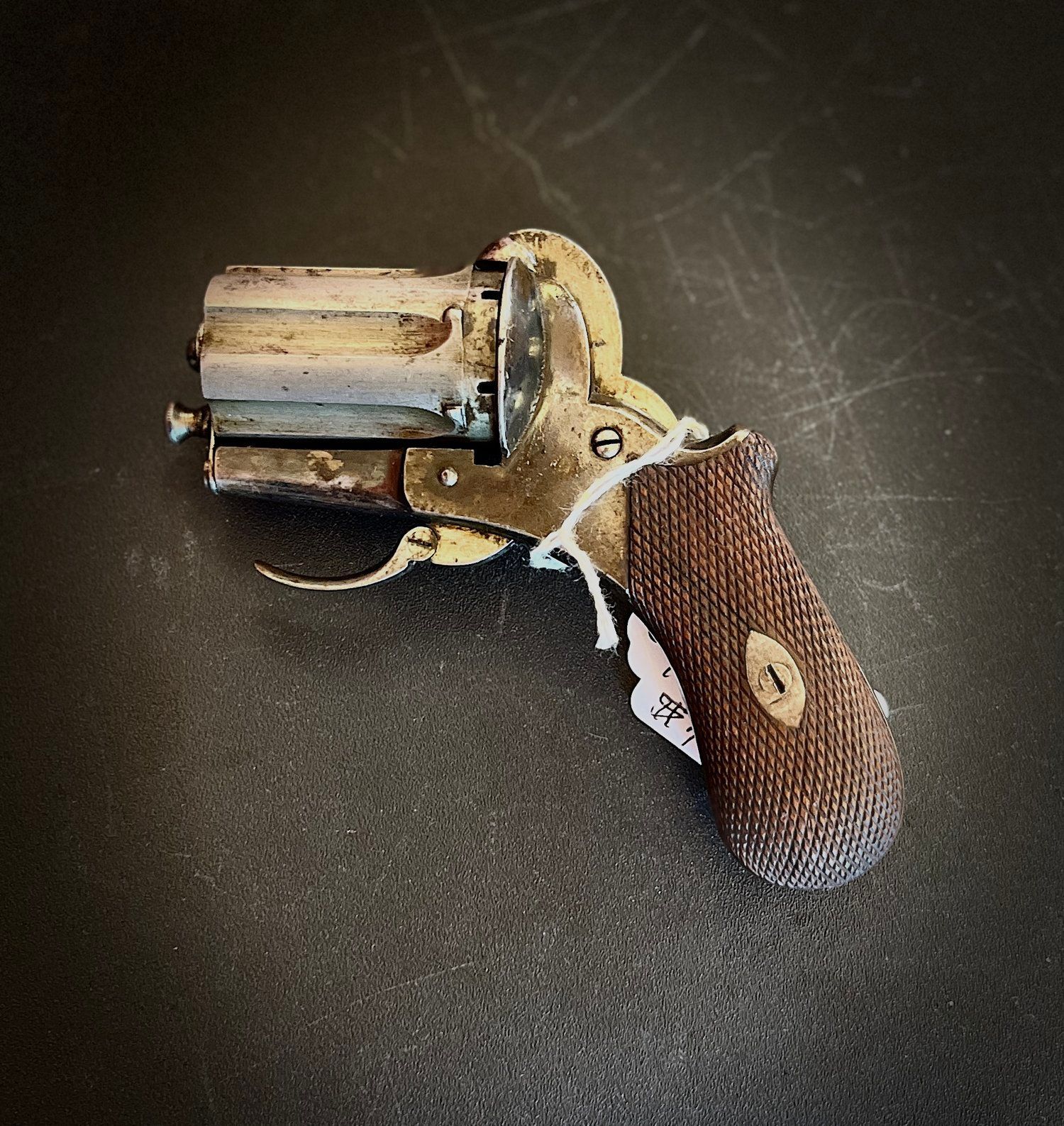 Antique revolver on a dark surface. The gun is silver with a brown grip and has a price tag attached.