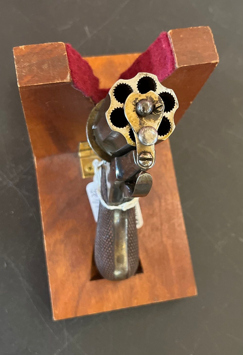 Antique revolver on a dark surface. The gun is silver with a brown grip and has a price tag attached.
