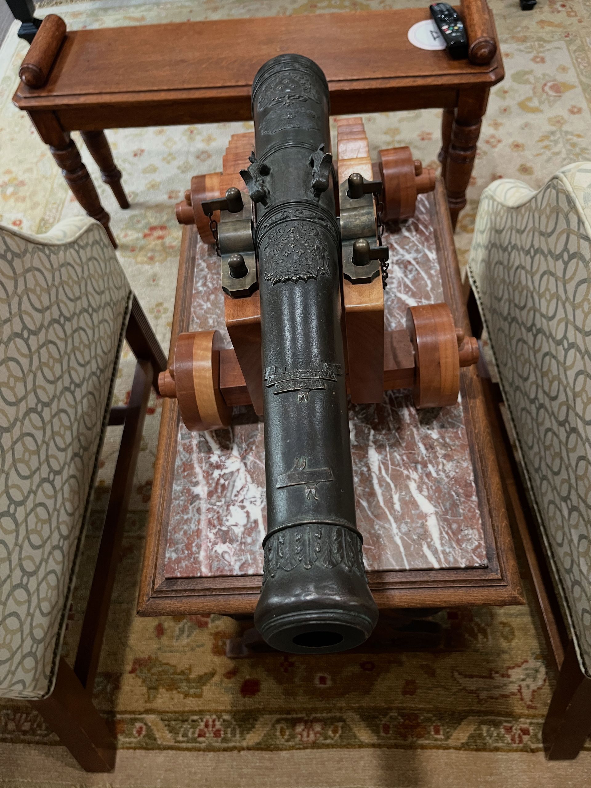 Ornate antique cannon on a marble-topped table, surrounded by chairs and a wooden table.