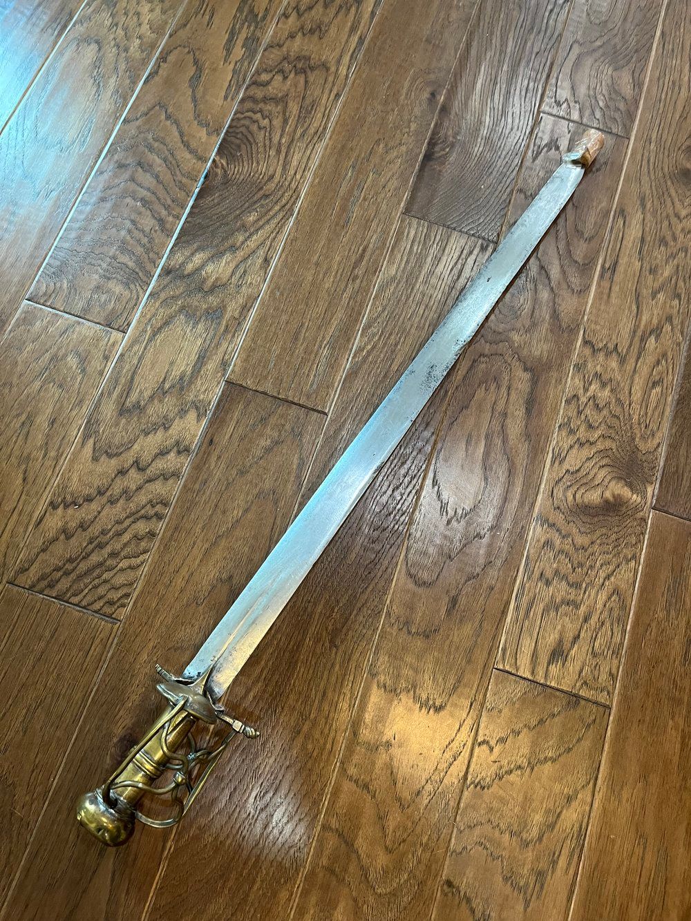 A decorative sword with a golden handle and a silver blade rests on a wooden floor.