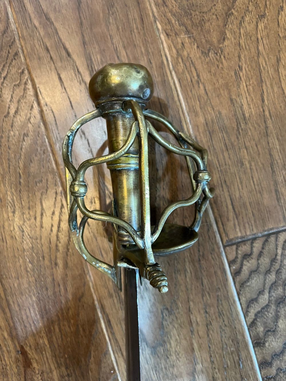 A decorative sword with a golden handle and a silver blade rests on a wooden floor.