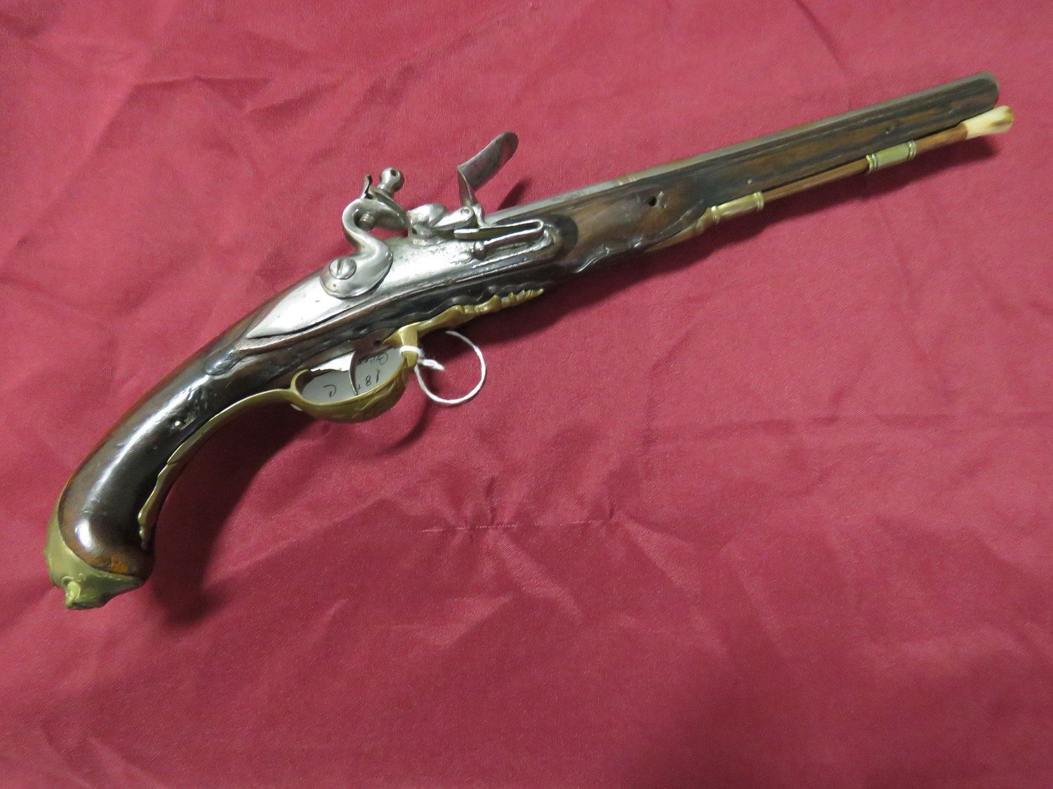 Antique flintlock pistol, dark wooden grip, ornate metalwork, resting on a red cloth surface.