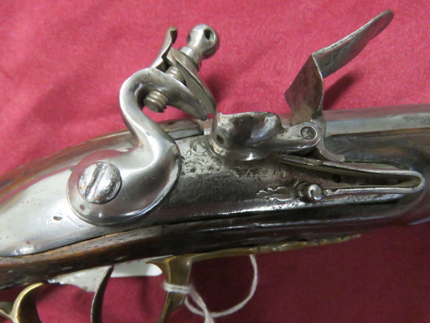 Antique flintlock pistol, dark wooden grip, ornate metalwork, resting on a red cloth surface.