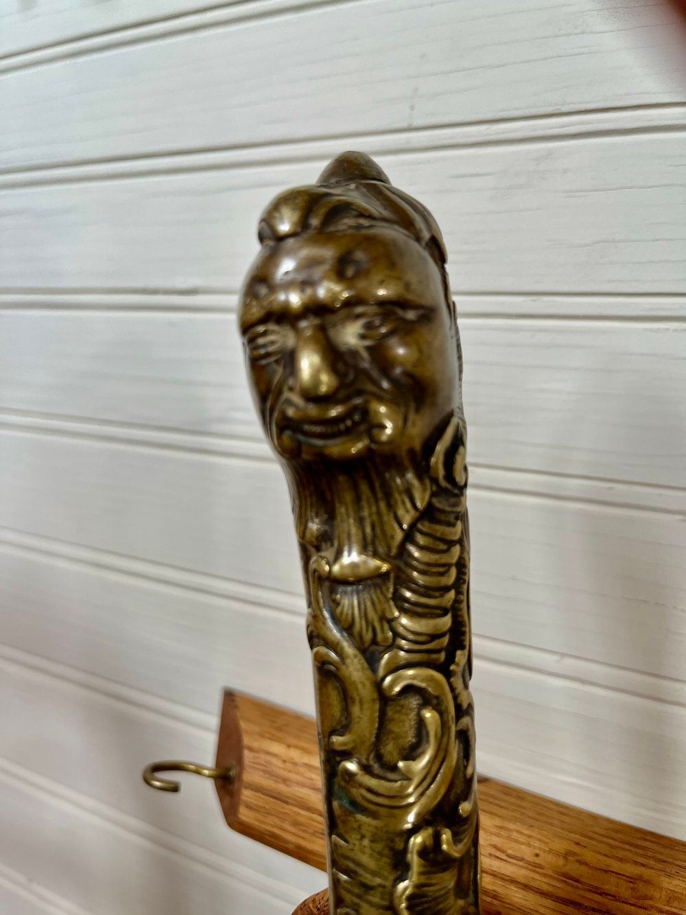 Ornate bronze sword hilt with a face on top and scrollwork details, mounted on a wooden rack.