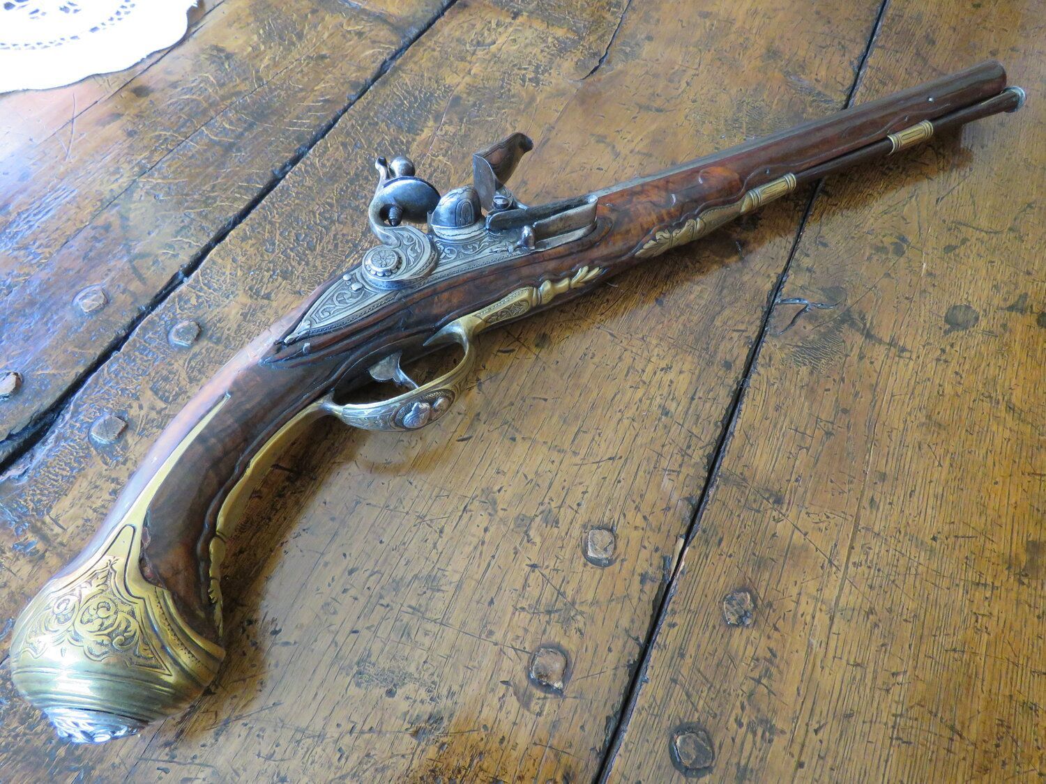 An ornate antique pistol with a wood and metal design, resting on a wooden table.