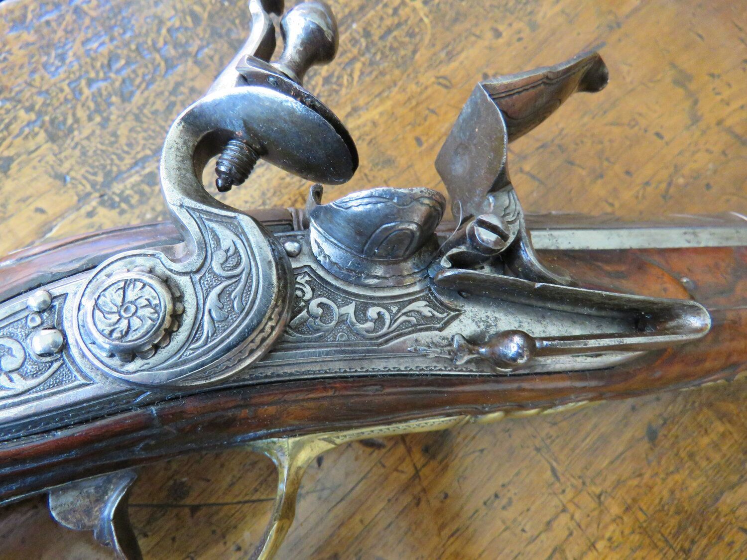 An ornate antique pistol with a wood and metal design, resting on a wooden table.