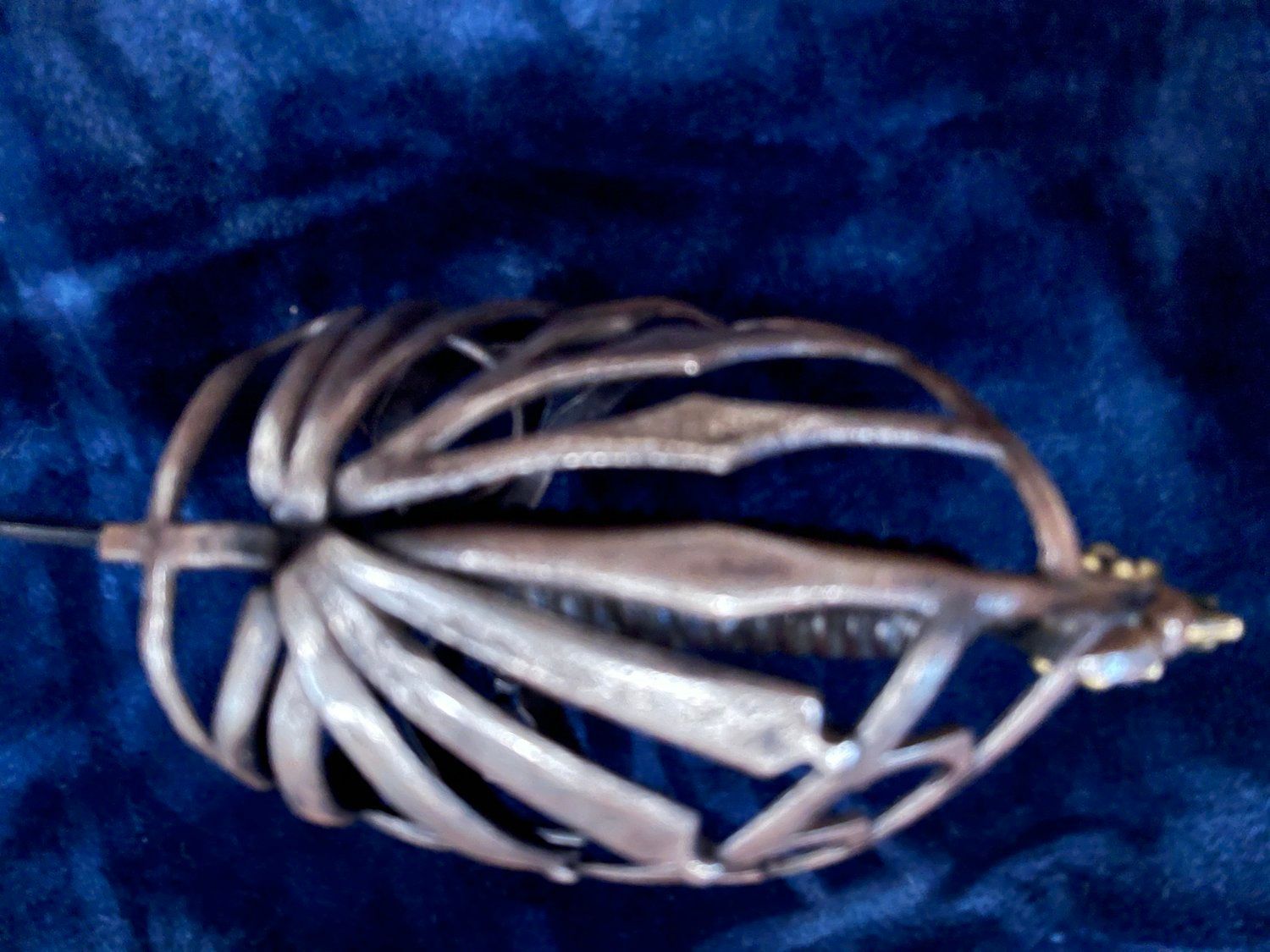 A silver saber with an ornate hilt on a wrinkled blue velvet surface.