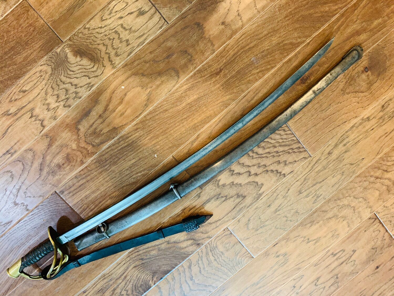 Antique sword with a wooden handle and scabbard lying on a wooden floor.