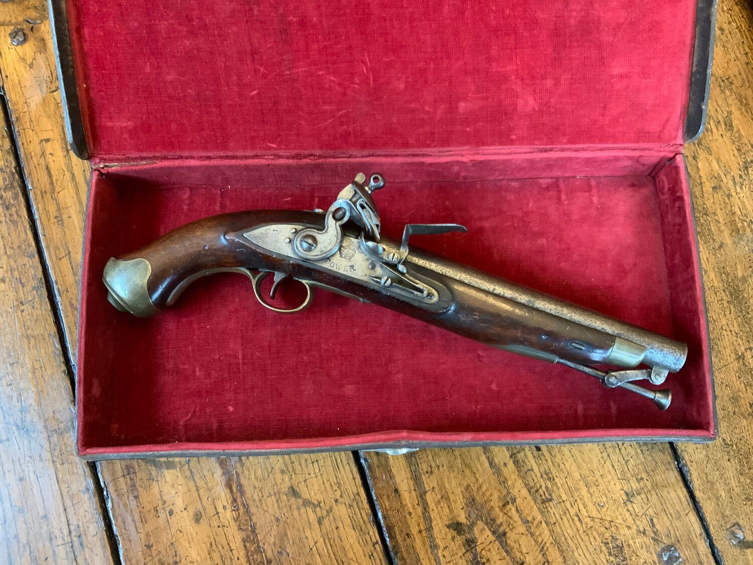 An antique pistol is sitting in a red box on a wooden table.