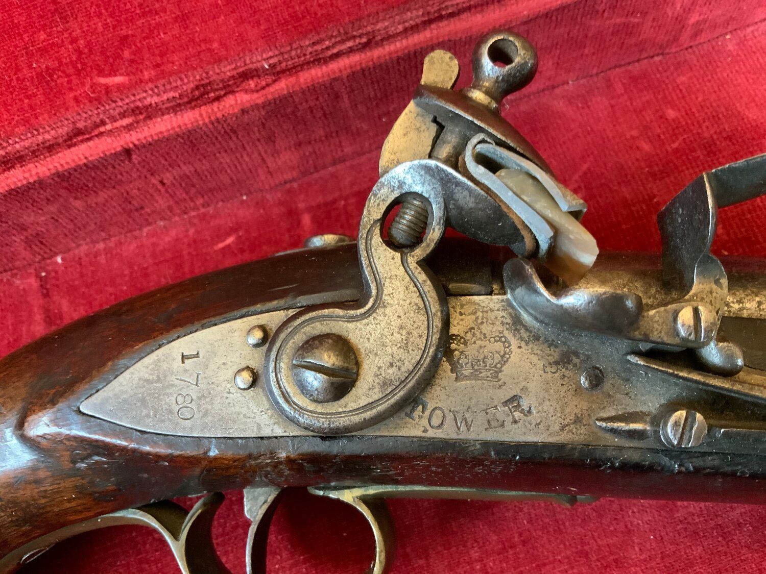 An antique pistol is sitting in a red box on a wooden table.