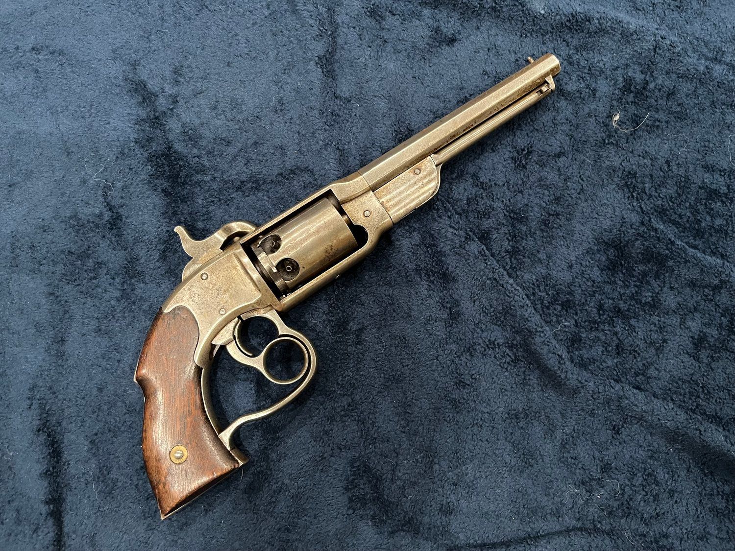 A small brass revolver with a wooden grip is sitting on a blue blanket.