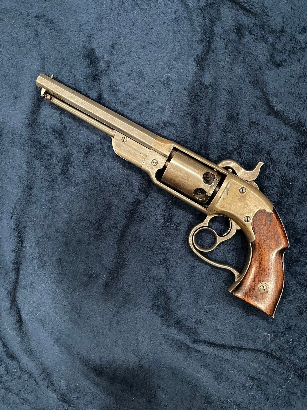 A small brass revolver with a wooden grip is sitting on a blue blanket.