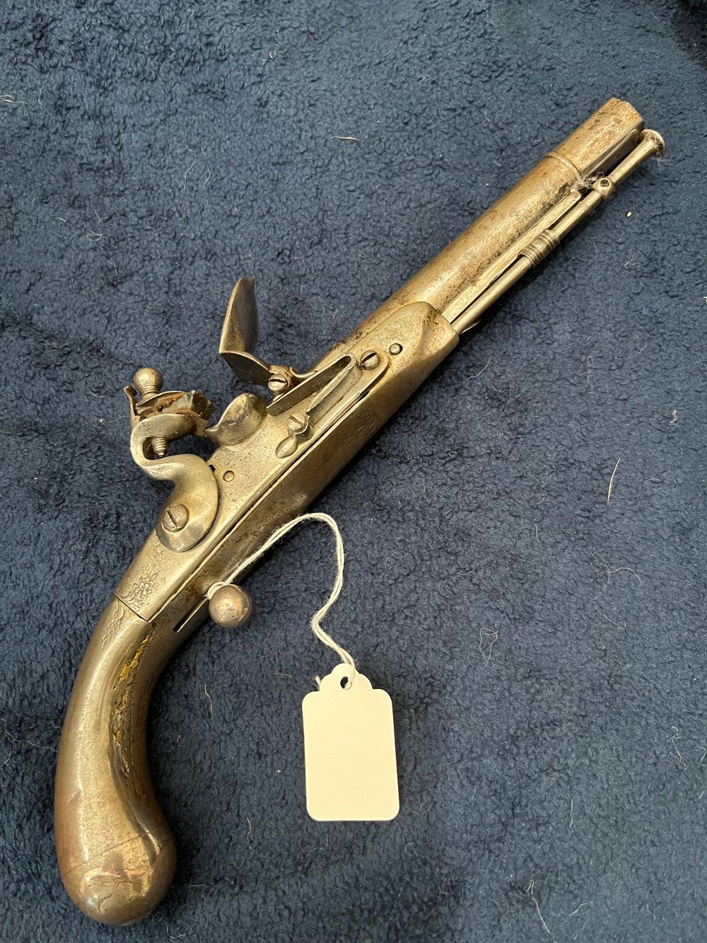 A brass pistol with a tag attached to it is sitting on a carpet.