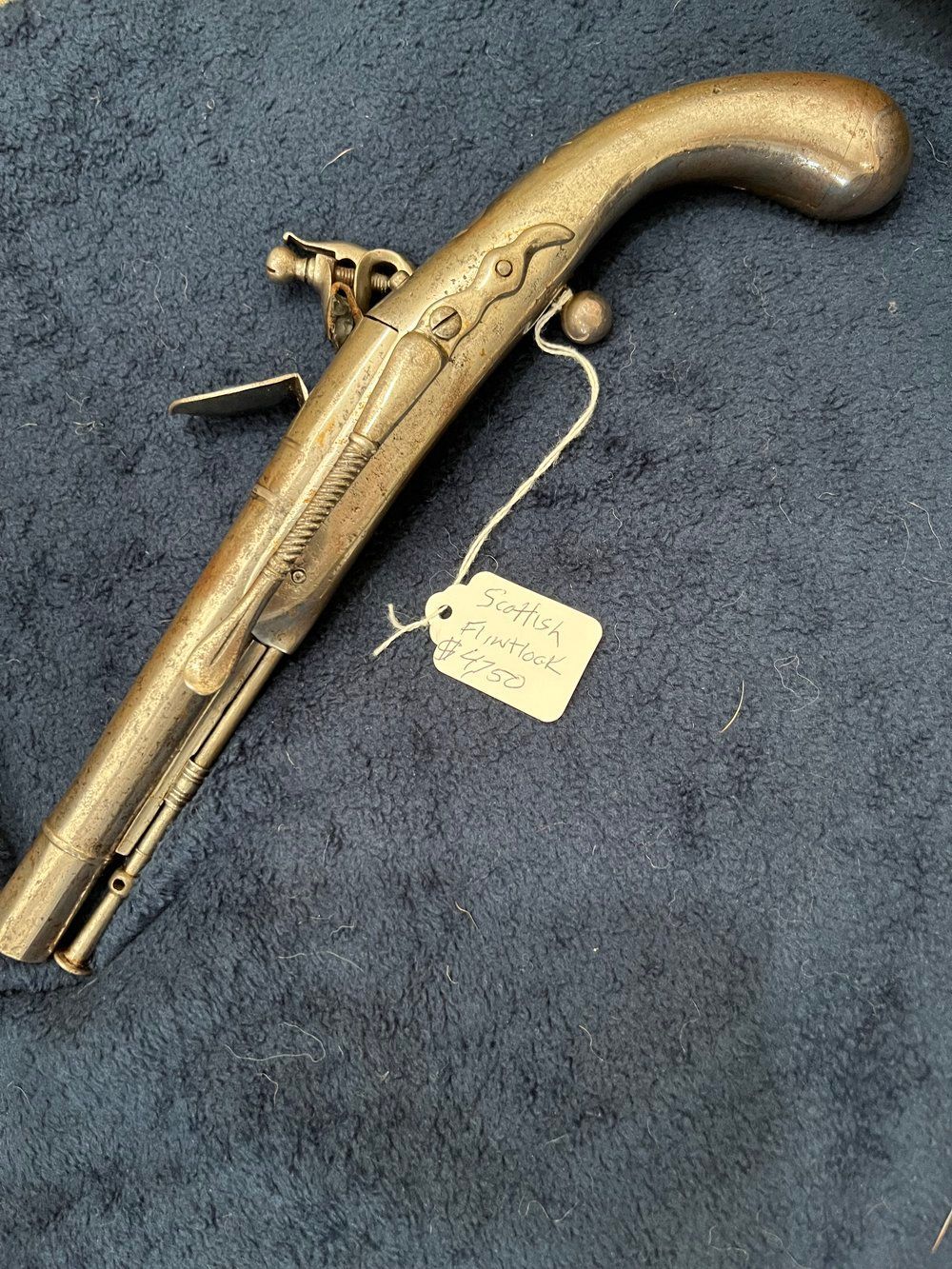 A brass pistol with a tag attached to it is sitting on a carpet.