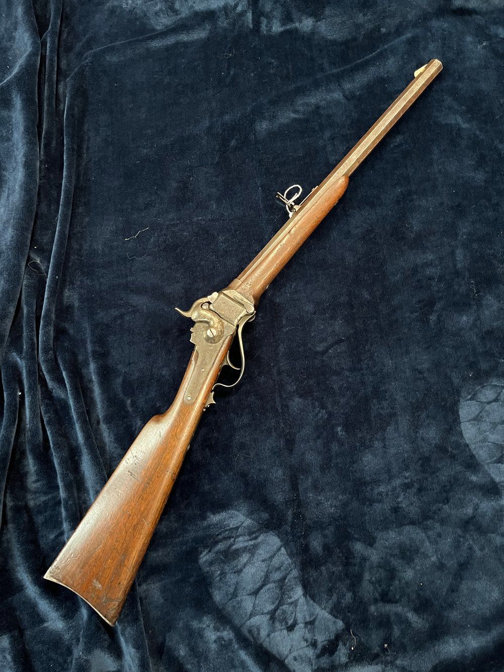 A rifle with wooden stock and metal barrel and details lies on a dark blue fabric surface.