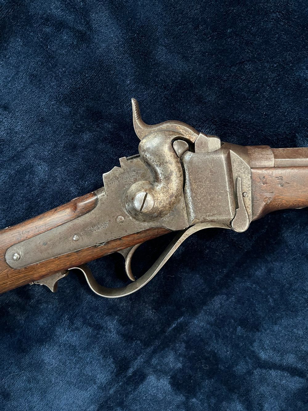 A rifle with wooden stock and metal barrel and details lies on a dark blue fabric surface.