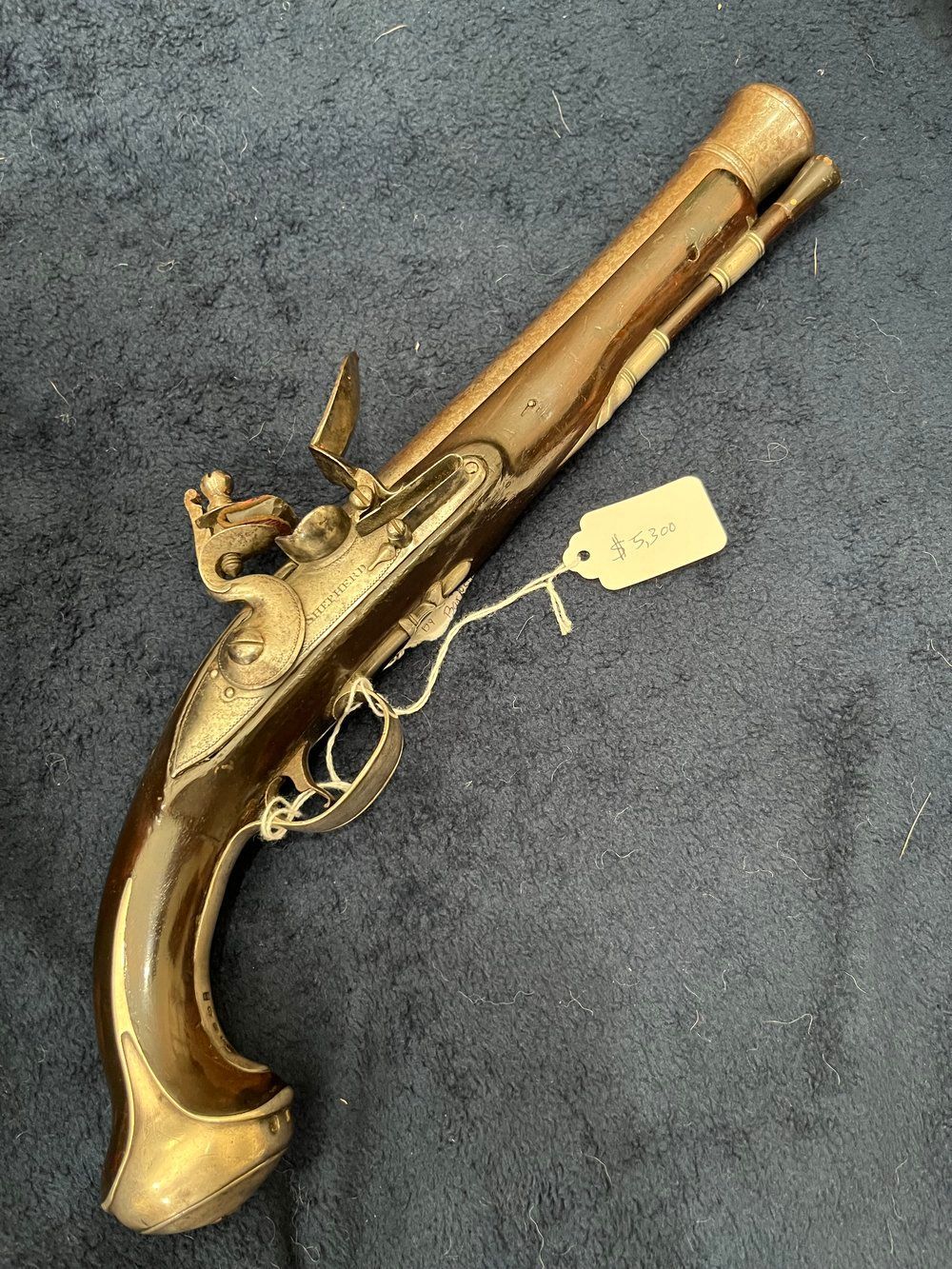 Antique flintlock pistol with ornate metal detailing and a wooden handle, resting on a dark blue surface.