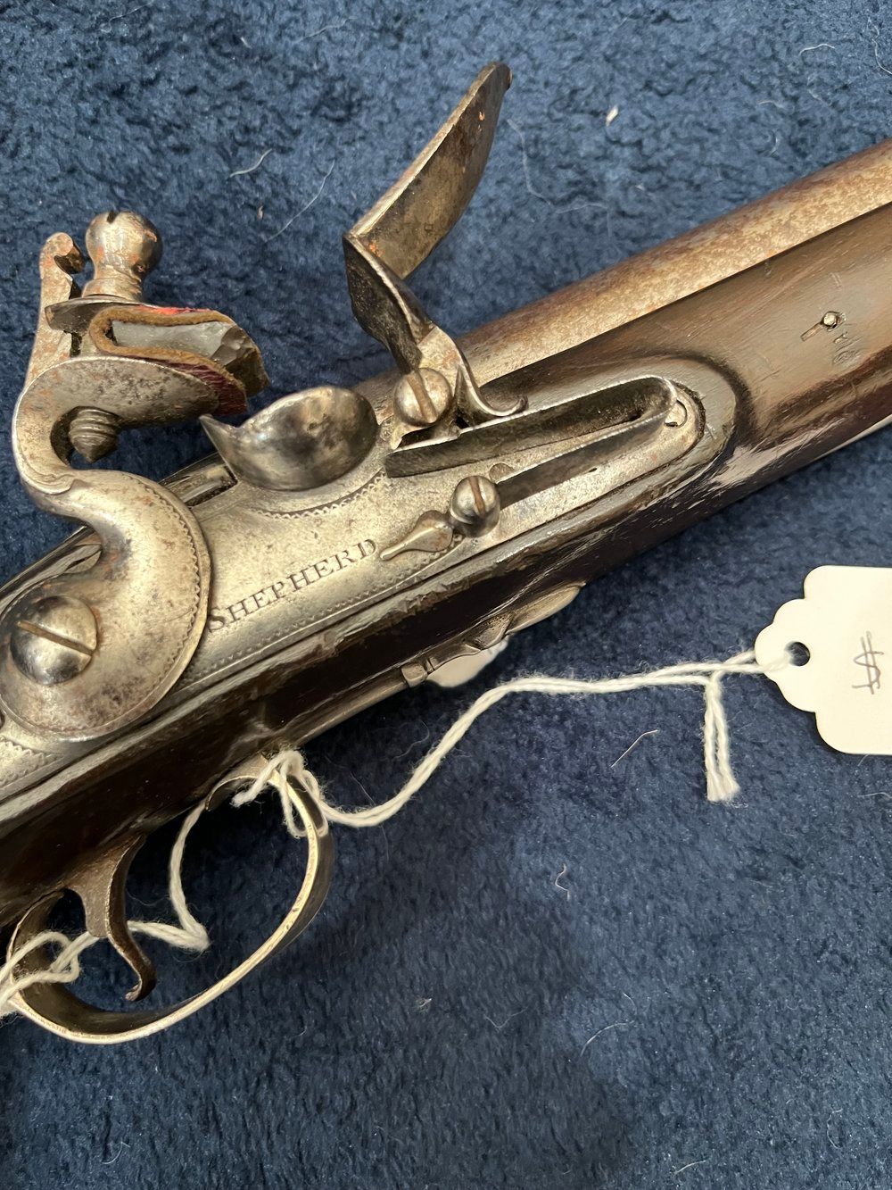 Antique flintlock pistol with ornate metal detailing and a wooden handle, resting on a dark blue surface.