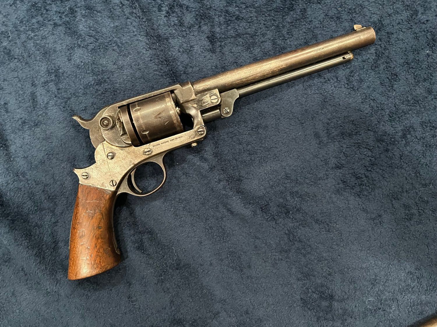 An old revolver with a wooden grip is sitting on a blue cloth.