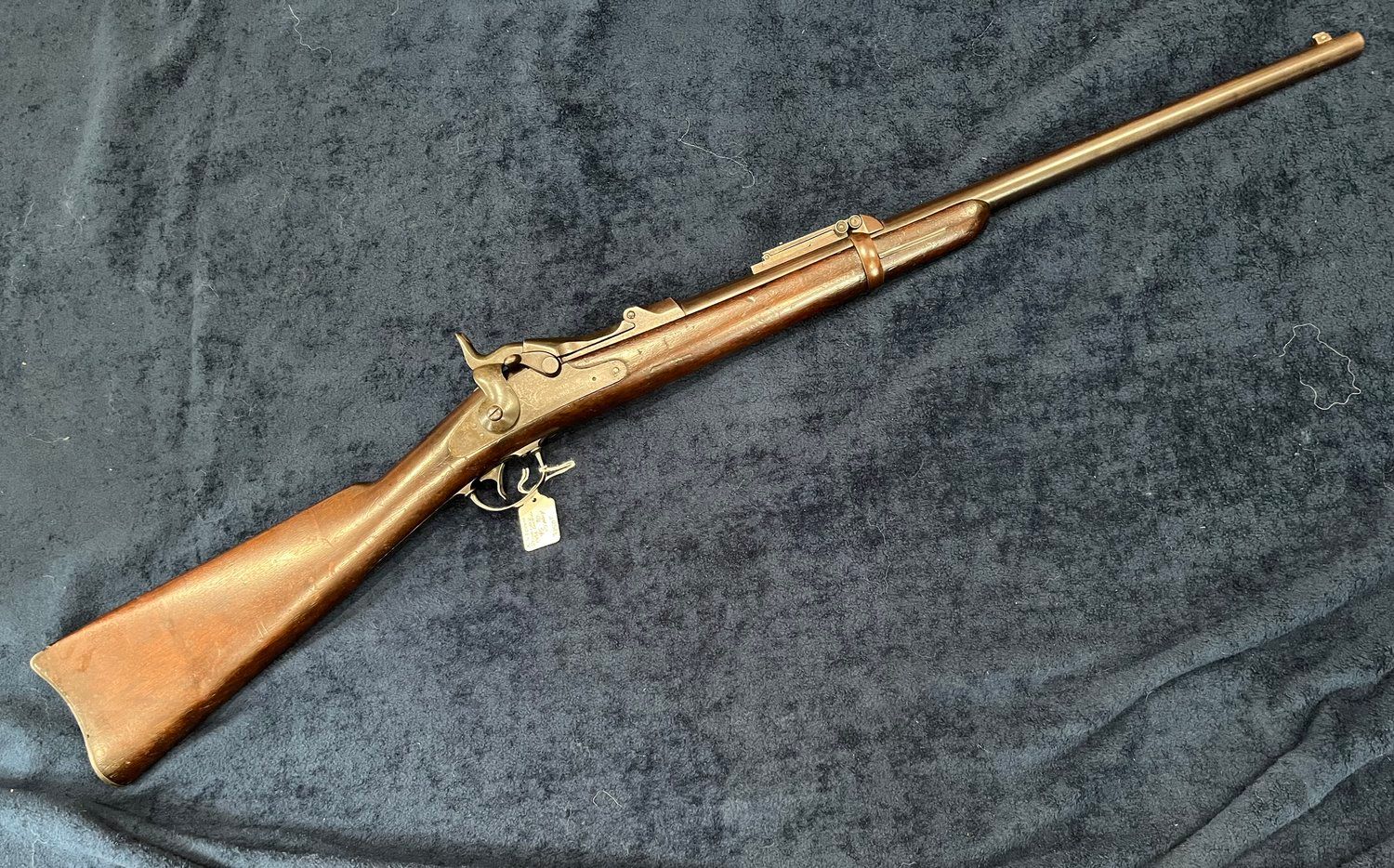 Antique rifle resting on a dark blue surface. It is brown with a long barrel, a wooden stock, and metal components.