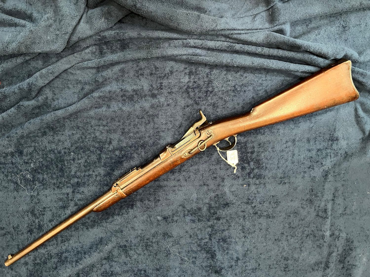 Antique rifle resting on a dark blue surface. It is brown with a long barrel, a wooden stock, and metal components.