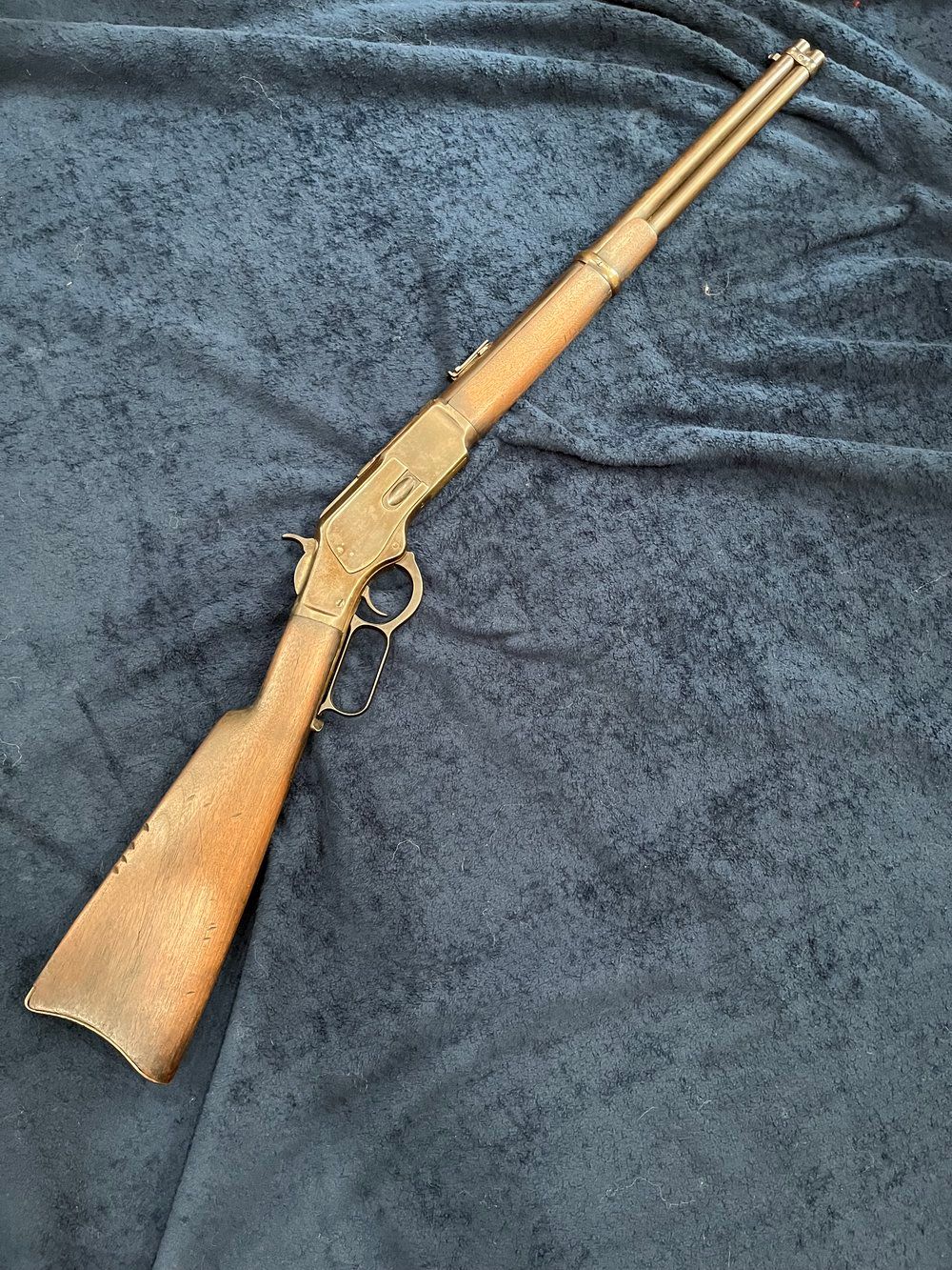 Lever-action rifle with wooden stock and metal components, laid on a dark blue textured surface.