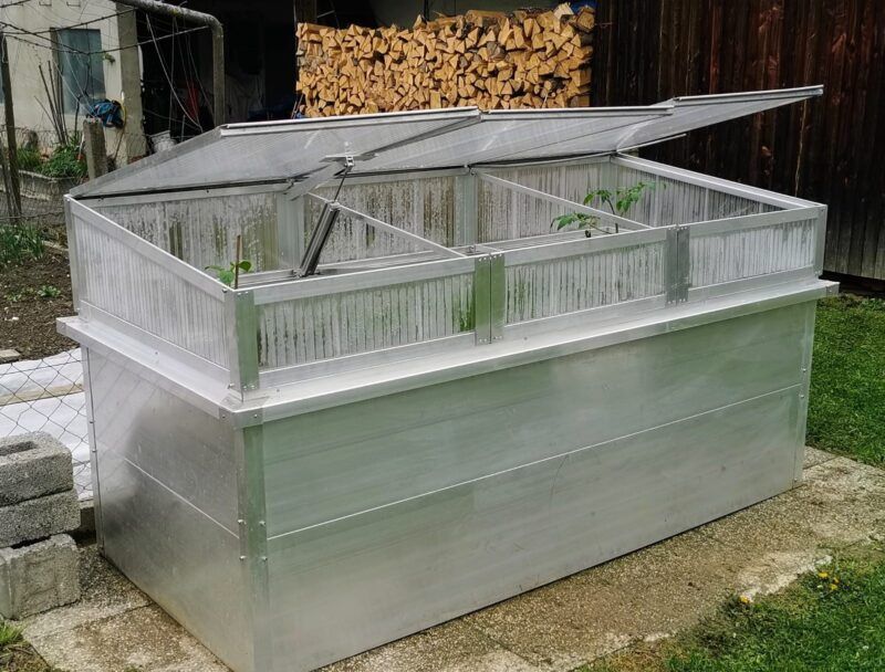 Ein erhöhtes Metallbeet mit transparenten Klappdeckeln für den Außenbereich.