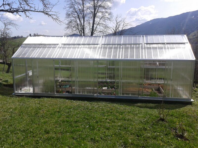 Gewächshaus auf einer Rasenfläche mit Bergkulisse.
