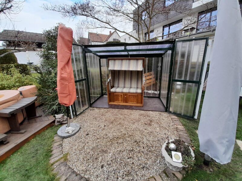 Überdachter Sitzbereich im Freien mit Strandstuhl, Kiesboden und Sonnenschirm.
