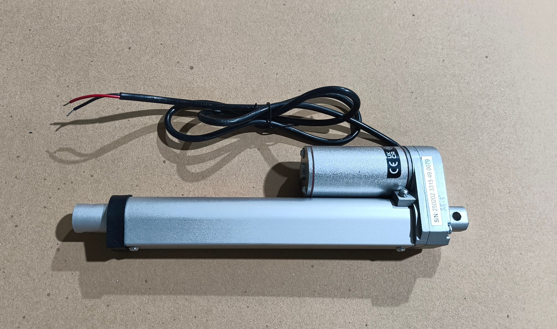 Silberner Linearantrieb mit schwarzen Drähten und Motor auf brauner Oberfläche.