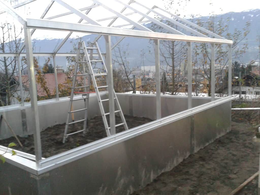 Gewächshausrahmen aus Aluminium mit innenliegender Leiter auf einer leicht erhöhten Plattform.