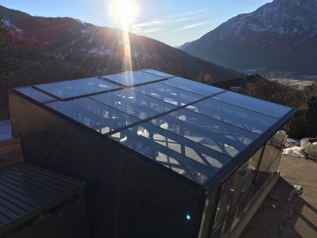 Glasdachkonstruktion mit Bergkulisse und strahlendem Sonnenschein.