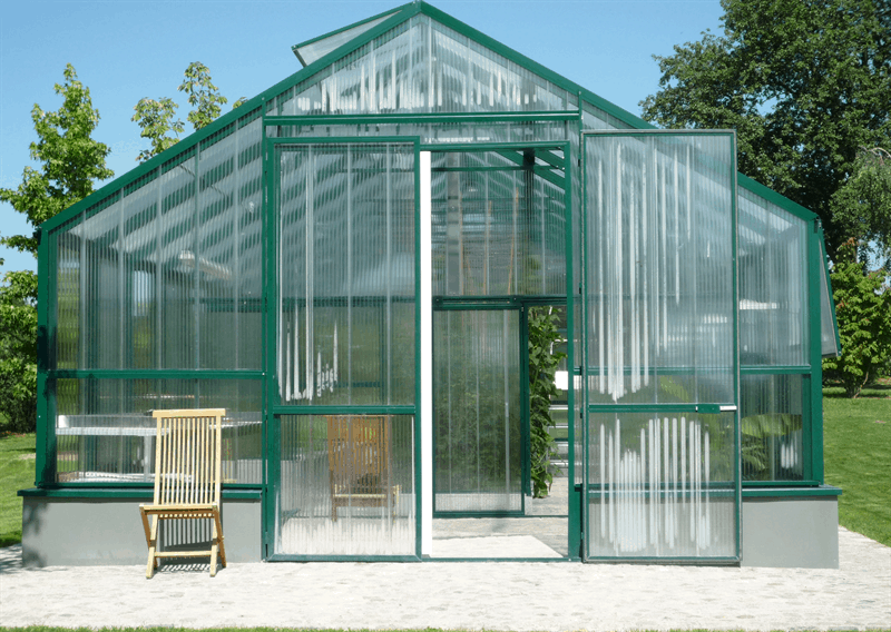 Grünes Gewächshaus mit offenen Türen, einem hellen Stuhl im Inneren und einer grasbewachsenen Außenanlage.