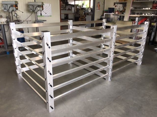 Zwei rechteckige Aluminiumregale mit horizontalen Streben, vermutlich zur Aufbewahrung, in einer Werkstatt.
