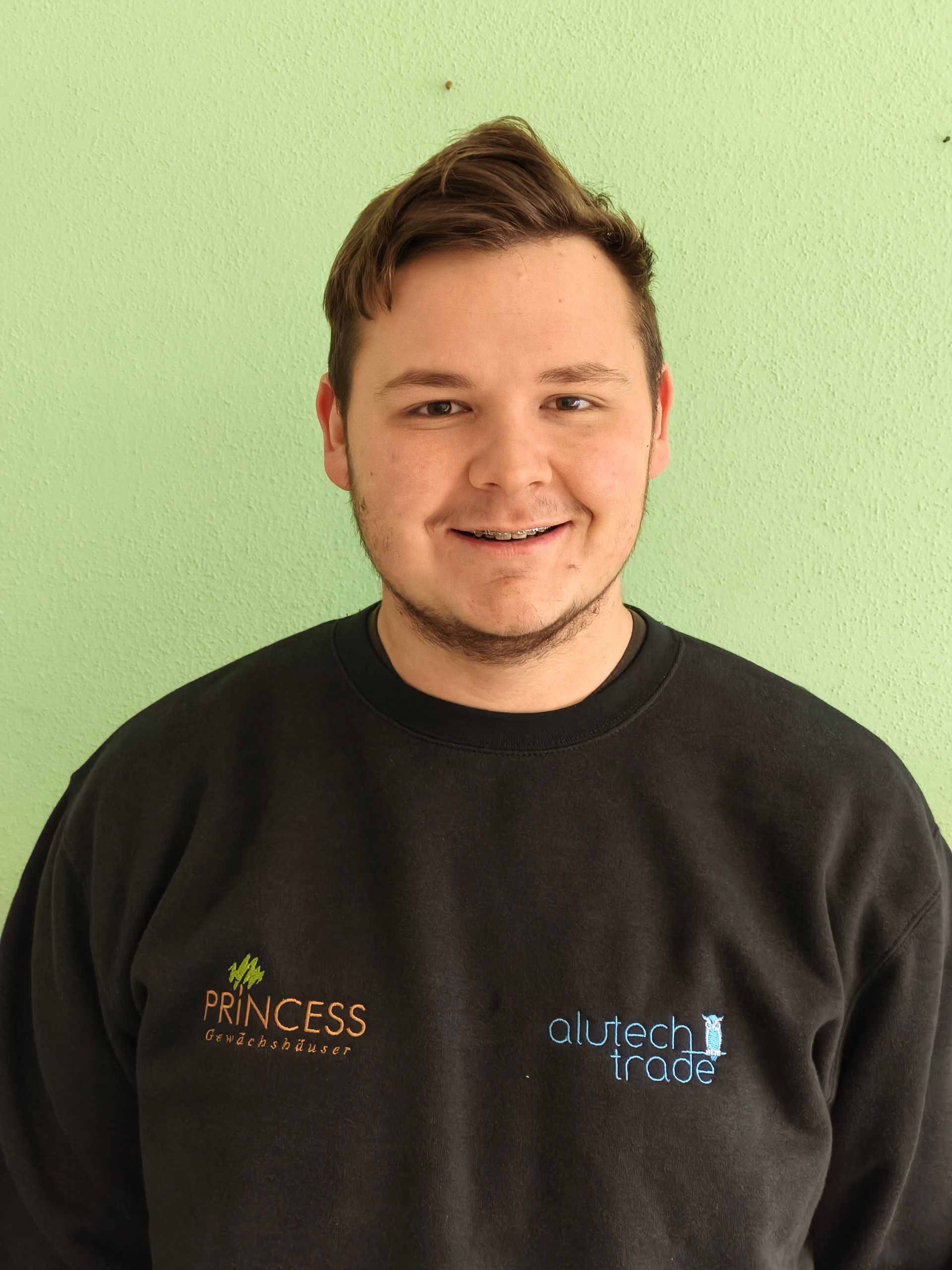 Frau mit Brille und langen Haaren in einem schwarzen Hemd posiert vor einer grünen Wand.