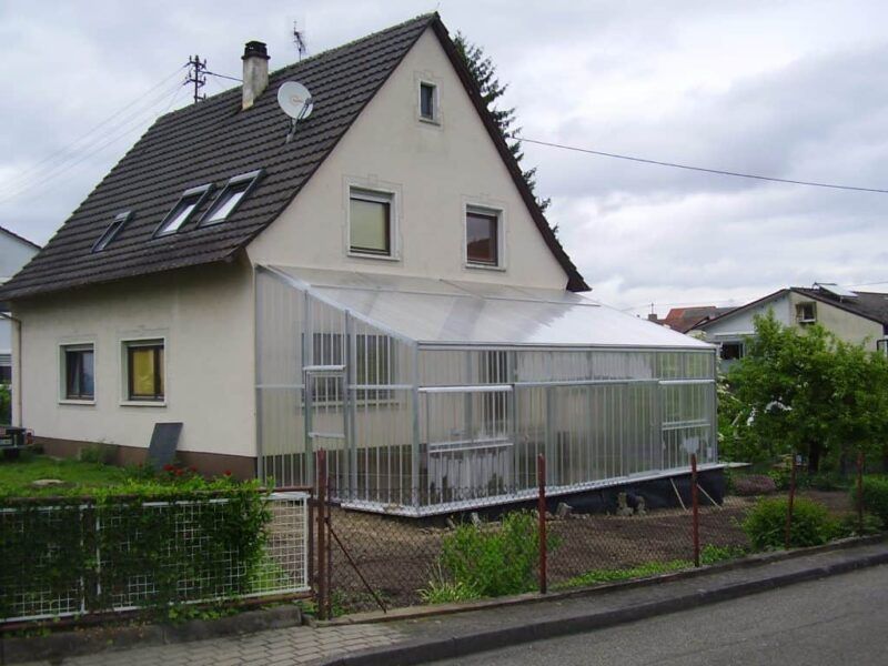 Ein Haus mit einem großen, lichtdurchfluteten Wintergarten an der Seite, darüber bewölkter Himmel.