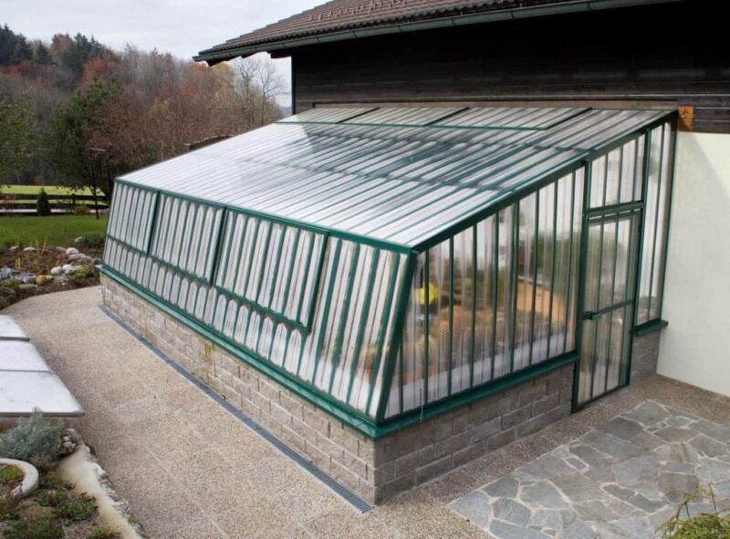 Gewächshaus an einem Gebäude angebaut, schräges Dach, Klarglas, Ziegelsockel, Außenlage.