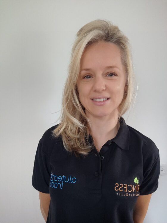 Frau mit blonden Haaren, die ein schwarzes Poloshirt trägt, lächelt in die Kamera.