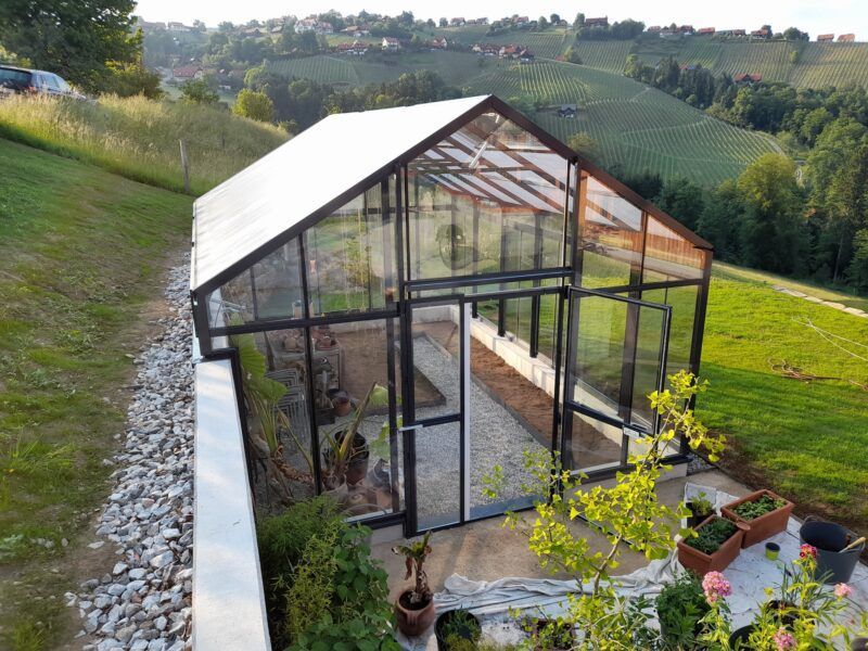 Gewächshaus mit Glaswänden und -dach in grasbewachsener Hanglage.